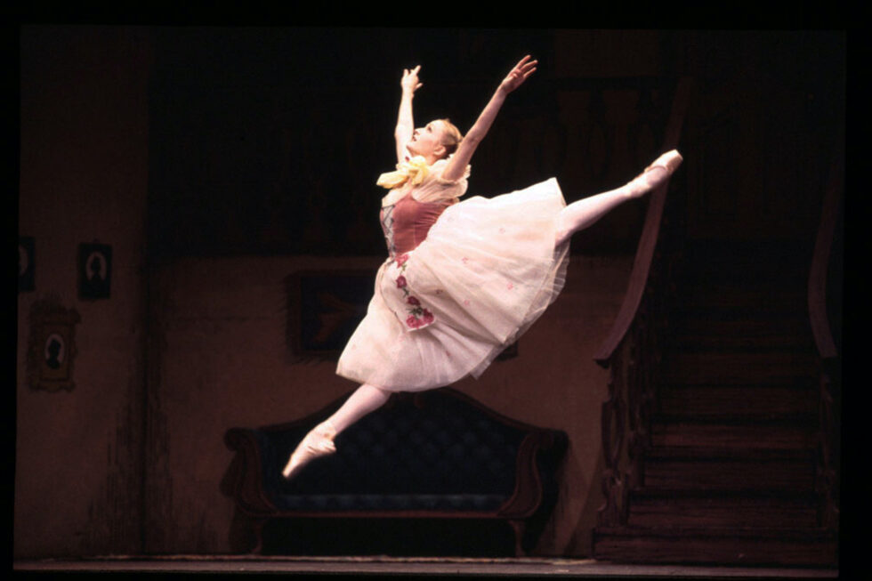 Murphy, wearing a knee-length pink tutu, does a large sissone. She looks up, holding her arms in a V-shape.
